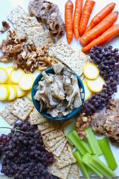 a platter with crackers, carrots, celery, grapes and other foods