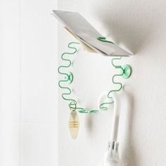 a white wall with a green string attached to it and a paper clip hanging from the side