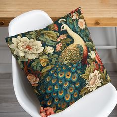 a peacock pillow sitting on top of a white chair next to a wooden table with flowers