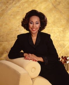 a woman sitting on top of a white chair next to a wall with gold paint