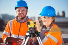 two people wearing hard hats are looking at something on a tripod while holding a camera