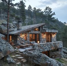 a small stone cabin on the side of a mountain with seating and lights lit up