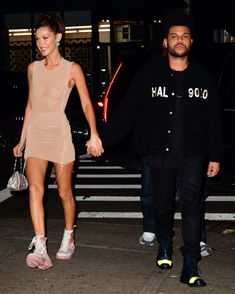 a man and woman walking across a street holding hands