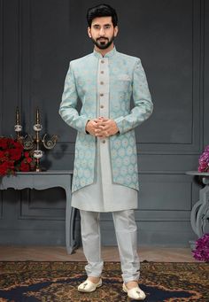 a man standing in front of a floral arrangement wearing a white sherwanit