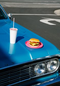 a plate with a hot dog and drink on it sitting on the hood of a blue car