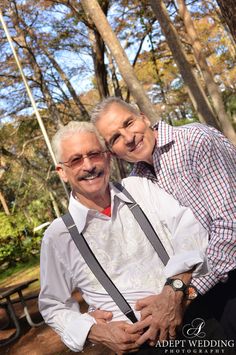 an older man and woman are posing for a photo in front of some trees with their arms around each other