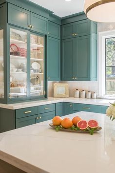 a kitchen with green cabinets and white counter tops, including grapefruits on a tray