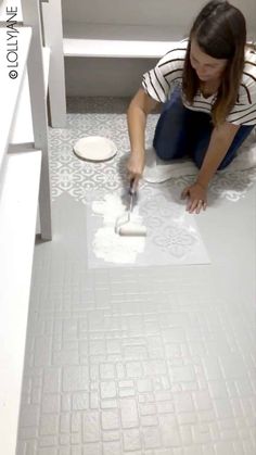 a woman kneeling down on the floor with a paint roller in her hand and painting tiles