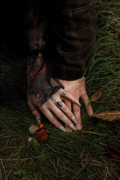 two hands holding each other with tattoos on their arms and fingers, in the grass