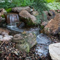 there is a small waterfall in the middle of some rocks and plants on the ground