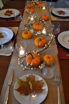 the table is set for thanksgiving dinner with candles and pumpkins on it's place mats