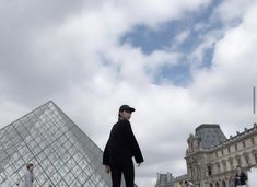 a man standing in front of a very tall glass pyramid with people walking around it