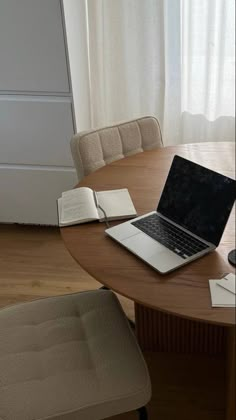 an open laptop computer sitting on top of a wooden table next to a book and chair