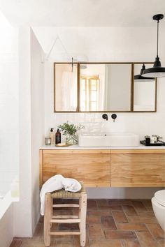 a bathroom with a wooden stool and two mirrors on the wall above it, next to a white toilet