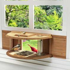 two birds sitting on top of a bird feeder in front of a window with trees outside