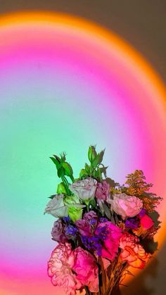 a vase filled with pink and white flowers on top of a table next to a rainbow colored wall