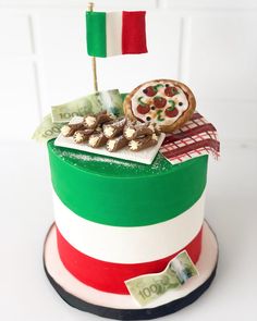 a multi - colored cake decorated with italian food and flag decoration on top, sitting on a table