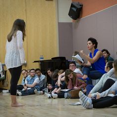 a group of people sitting on the floor in front of a woman with a microphone