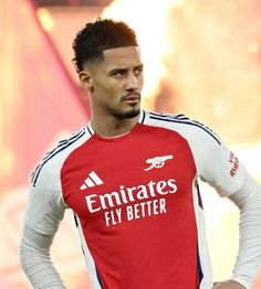 a man standing with his hands on his hips wearing a red and white shirt that says emirates fly better