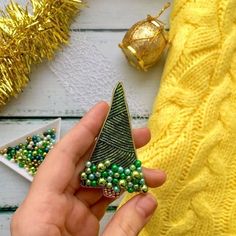 a hand holding a green beaded christmas tree brooch in front of a yellow sweater