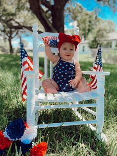 Smiley Baby girl in a navy blue shirt and tank top outfit with white stars and an oversized red bow sitting in a white rocking chair in front of a tall big tree with USA flags and red white and blue flowers 4th Of July Pics, 4th Of July Photography, Diy Newborn Photography, 4th Of July Photos