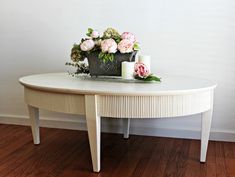 a table with flowers and candles on it in front of a white wall next to a wooden floor