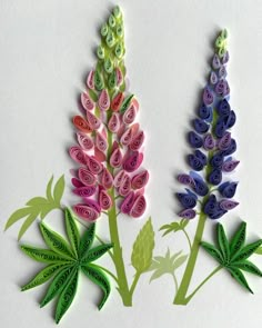 three different colored flowers made out of paper on a white surface with green stems and leaves