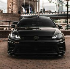 a black volkswagen car parked in front of a bridge on a brick road next to a tall building