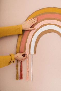 two hands are holding the ends of a rainbow wall hanging