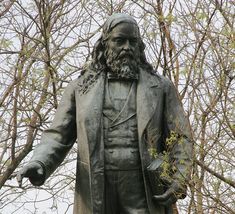 a statue of a man with long hair and beard standing in front of some trees