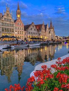 boats are docked in the water next to some buildings and flowers on the side of the river