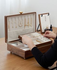 a woman sitting at a wooden table with an open jewelry box on top of it