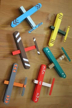 several different colored wooden toy airplanes sitting on top of a wood table next to each other