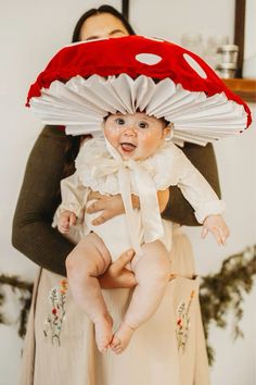 a woman holding a baby wearing a red and white umbrella hat on top of her head