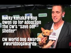 a man is holding a small dog in his lap and talking to someone else on the red carpet