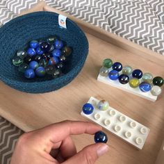 a person is playing with some marbles on a wooden tray in front of a blue bowl