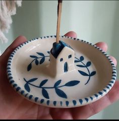 a hand holding a blue and white bowl with a toothpick in the shape of a house