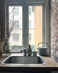 a kitchen sink sitting under a window next to a brick wall