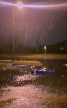 a car is sitting in the middle of a flooded street at night with its lights on