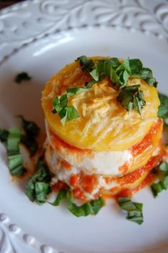 a white plate topped with lasagna covered in sauce and cheese, garnished with parsley