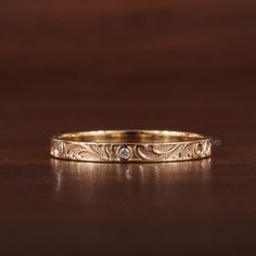 a gold wedding band that has been engraved with flowers and leaves on the side, sitting on a wooden surface