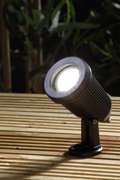 a light that is sitting on top of a wooden table next to some plants in the background