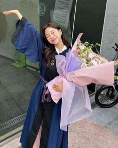 a woman in a graduation gown holding flowers and a large blue shawl over her shoulder