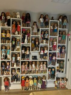 a room filled with lots of different types of dolls on shelving units and wooden floors