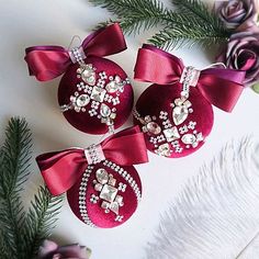 three red christmas ornaments with bows and jewels on them, surrounded by flowers in the background