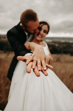 a bride and groom hugging in the middle of a field with their hands on each other