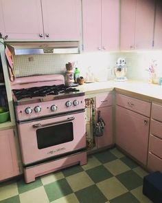 a pink stove top oven sitting inside of a kitchen next to wooden cabinets and drawers