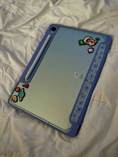 a blue tablet with stickers on it laying on a white sheeted surface next to a pen