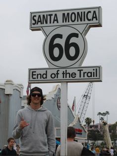 a man standing next to a sign that says santa monica 66 end of the trail