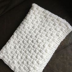 a white crocheted square sitting on top of a black leather couch next to a pillow